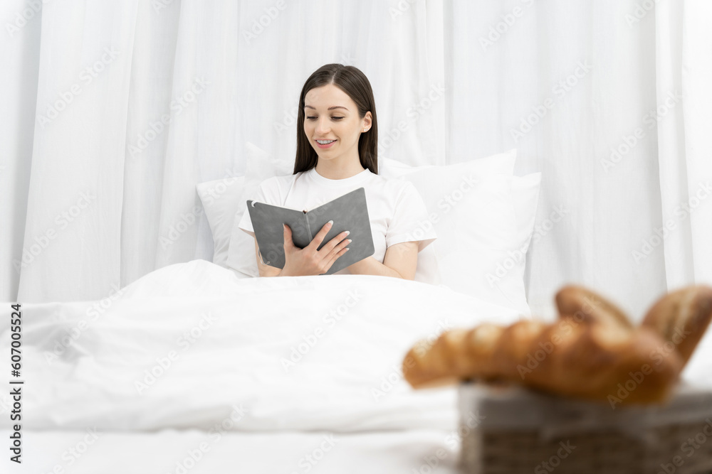 woman in the white shirt and pajama on a bed looking reading a book. woman in the white shirt and pajama on a bed looking reading a book.