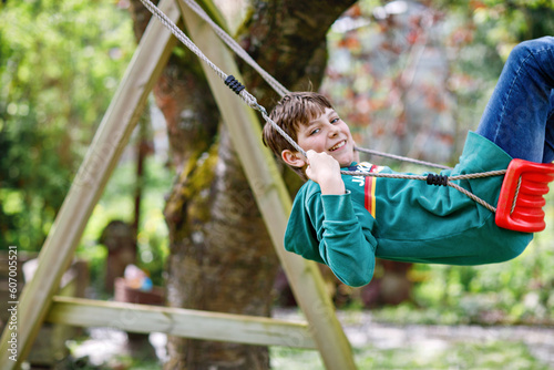 Happy school boy having fun on swing in domestic garden. Healthy child swinging under blooming trees on sunny spring day. Preteen Kid laughing and crying.