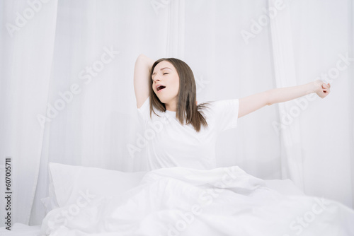 Woman is waking up and stretching in the bed in her bedroom.