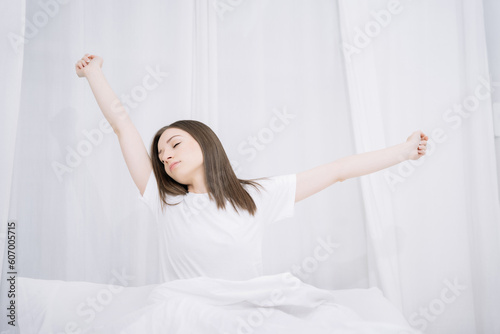 Woman is waking up and stretching in the bed in her bedroom.