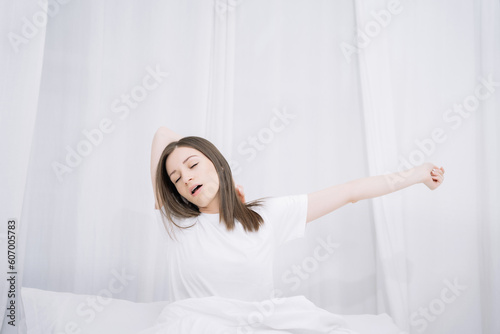 Woman is waking up and stretching in the bed in her bedroom.