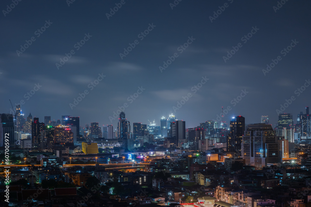 Fototapeta premium City scape night time of Bangkok, Thailand. on blue sky and cloud backgroundTall building in the night and line of light car in the extra road urban.Long exprossure.