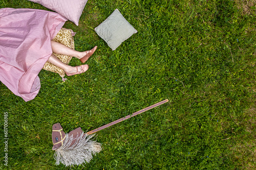 Top view of the legs of a girl in a pink dress, grass, pillows and a toy horse