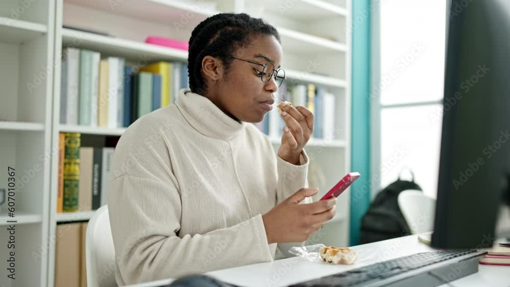 African american woman student using smartphone eating waffle at library university African american woman student using smartphone eating waffle at library university