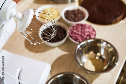 Selective focus on a whisk of food processor on the kitchen countertop with blurred organic dark  caramel  white and ruby pink chocolate chips. Ingredients for making glaze  sweet desserts  brownies