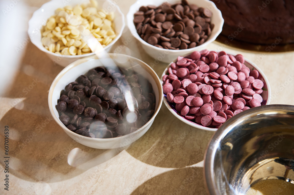 View through blurred whisk of a food processor of various chips of white, dark, ruby, and caramel organic chocolate in bowls on the kitchen countertop View through blurred whisk of a food processor of various chips of white, dark, ruby, and caramel organic chocolate in bowls on the kitchen countertop
