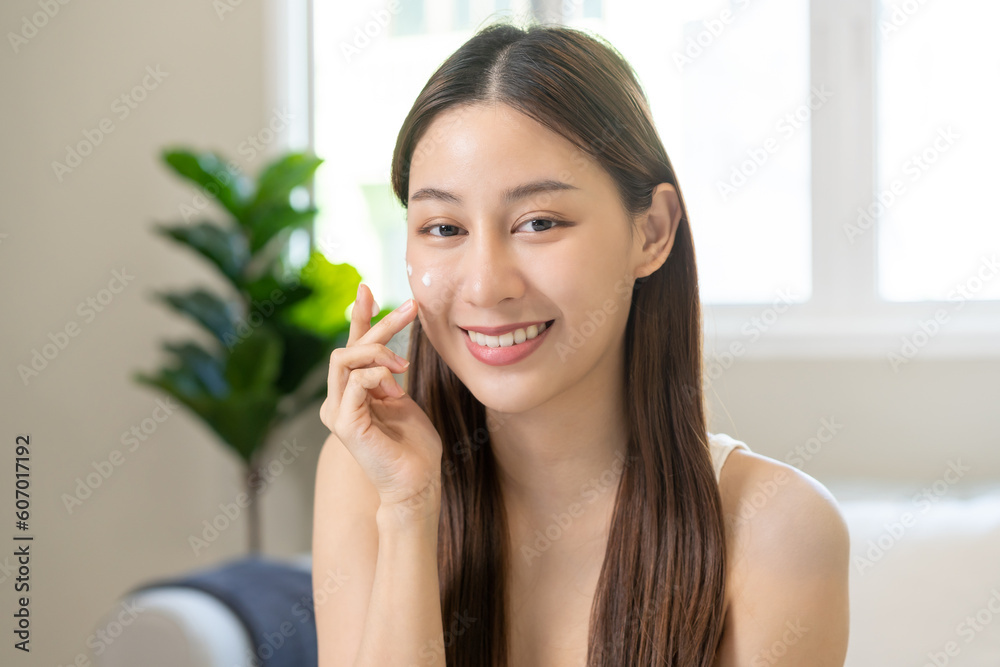 Fresh healthy skin, beautiful smile of asian young woman, girl looking at mirror, applying moisturizer on her face, putting cream treatment before makeup cosmetic routine at home. Facial Beauty. Fresh healthy skin, beautiful smile of asian young woman, girl looking at mirror, applying moisturizer on her face, putting cream treatment before makeup cosmetic routine at home. Facial Beauty.
