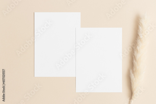 Two white invitation cards mockup with a pampas decoration on the beige table. 5x7 ratio, similar to A6, A5.