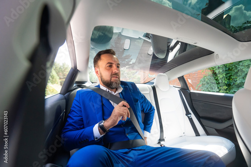 A caucasian man in a blue suit fastens his seat belt in the back seat of a car. Business class passenger. 