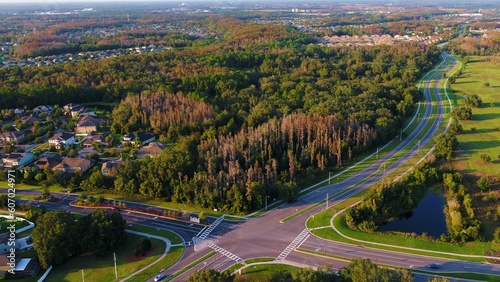 Aerial shot of a road surrounded by trees in summer with buildings in the background
