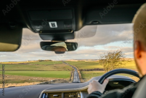 Man driving in the car on the empty countryside road alongside the green fields during the daytime