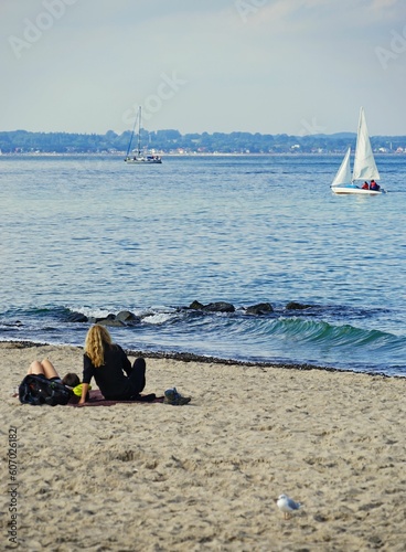 Photos Vertical back view of people resting on sandy Travemuende beach with sailboats i