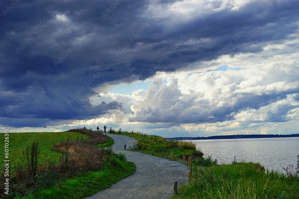 Image of a road in a field with a beautiful sky and a water surface on the right
