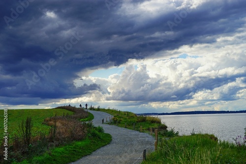 Image of a road in a field with a beautiful sky and a water surface on the right