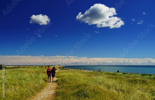 Image of a road surrounded with grass and people walking, the Baltic Sea on the right in Germany