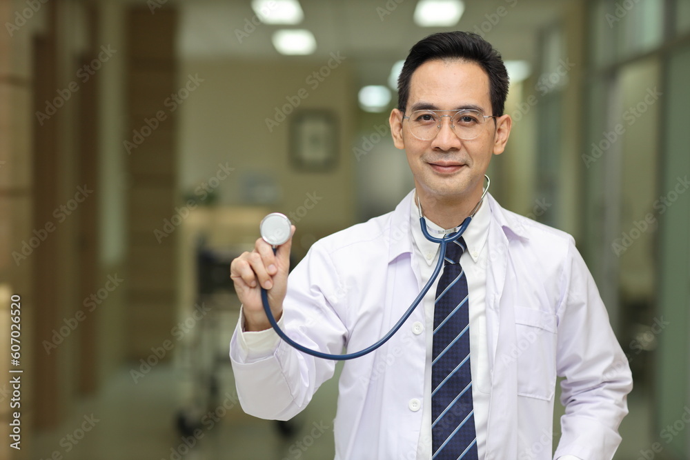 Happy asian medicine doctor standing and using stethoscope with hospital blurred background. Medical technology, treatment, healthcare and health insurance concept