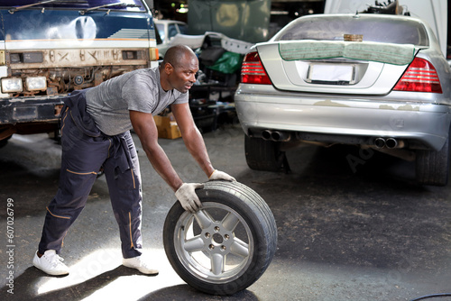 Man technician car mechanic in half uniform holding tire for replacement or changeing at repair garage. Happy asian worker smiling and looking at camera. Concept of car center repair service. © feeling lucky