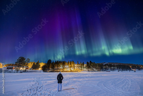 Young girl watching purple, blue and green Northern lights (aurora borealis) 
above Ounasjärvi lake in Hetta, Lapland, Finland