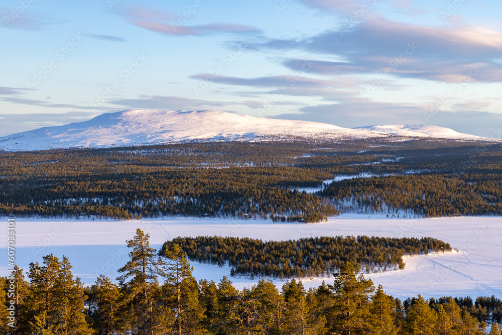 Bird's-eye view of the snow capped Pyhakero mountain in Lapland, Finland with a pine forest and frozen lake in the foreground