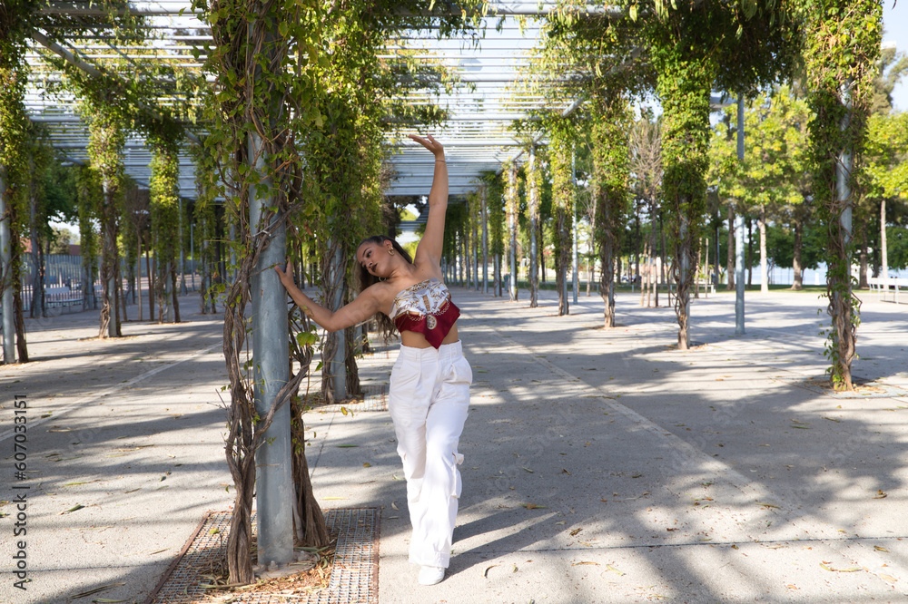 Latin woman, young and beautiful dancing modern dance in the street in a park and makes different expressions and postures. Concept dance, hip hop, dance, art, action, beauty, youth art.