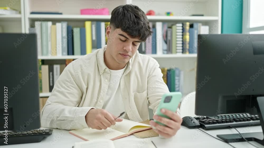 Young hispanic man student using smartphone writing notes at library university Young hispanic man student using smartphone writing notes at library university