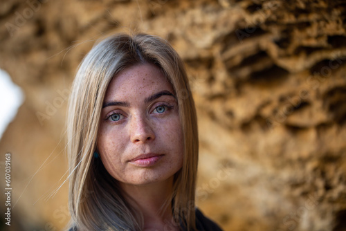 Close-up portrait of a girl with falling rays of the sun in nature with blue eyes and freckles, looking at the camera