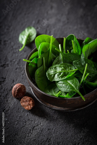 Green spinach in bworn rustic bowl on dark table