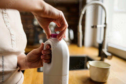 Girl opening bottle with milk juice beverage and take cup at kitchen. Woman with protein coctail drink at home