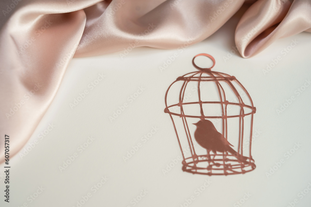 Pink paper cage with a bird on a background of pink silk draped fabric. Background picture for congratulations on the place for the inscription Pink paper cage with a bird on a background of pink silk draped fabric. Background picture for congratulations on the place for the inscription