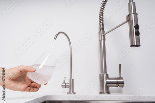 Woman get filtered water from stainless faucet into a glass