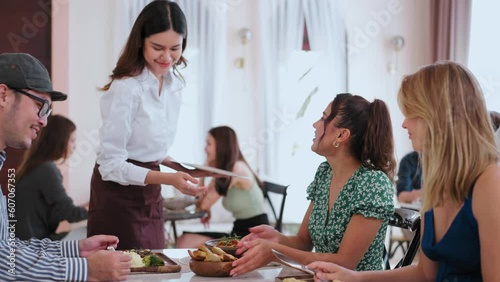 Cheerful waiter Asian woman serving and putting plate food to guests in restaurant, Service Food and Restaurant concept