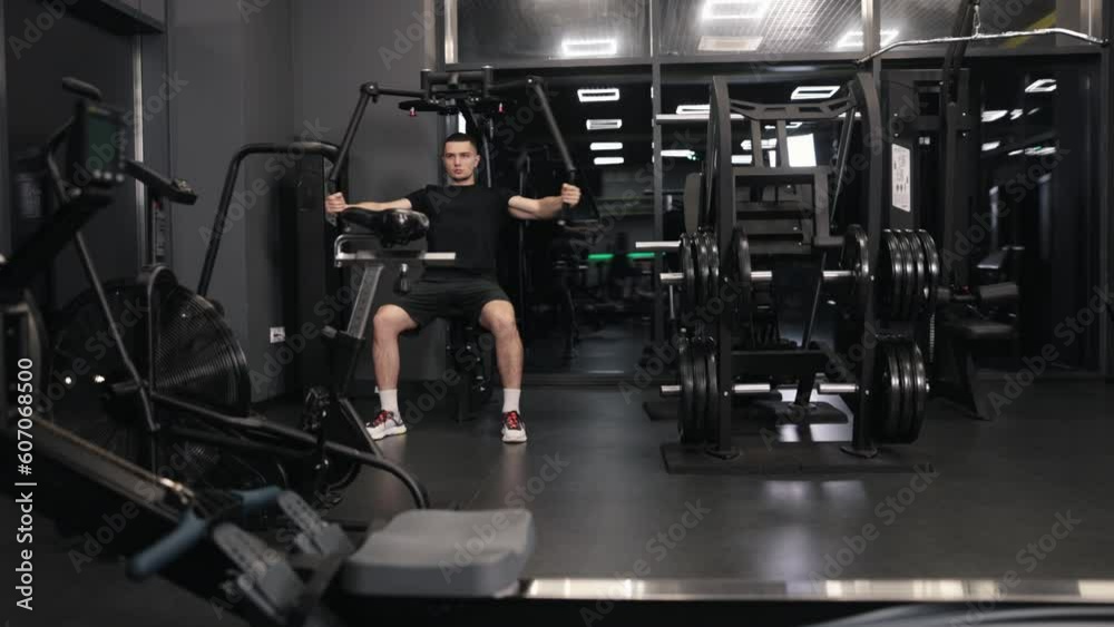 Workout machine, Dumbbell workouts, Pectoral muscles. Handsome, physically fit man works on building arm and chest muscles using exercise machine at fitness center. Workout machine, Dumbbell workouts, Pectoral muscles. Handsome, physically fit man works on building arm and chest muscles using exercise machine at fitness center.