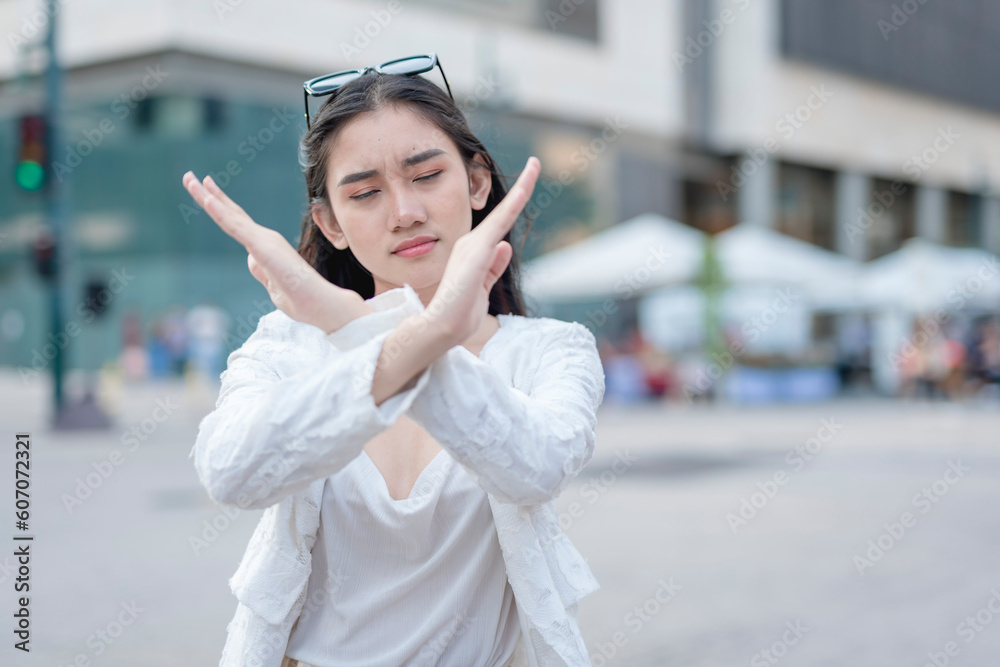 An adamant young woman say no, gesturing with an x mark with both arms. Rejecting an offer or feeling uncomfortable with someone. Focus on hand, Urban city setting.