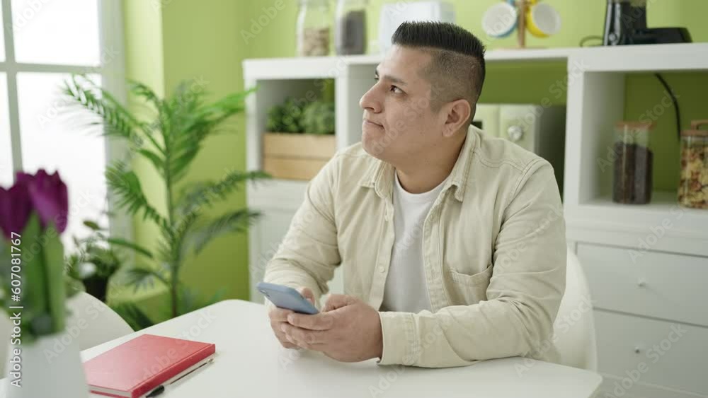 Young hispanic man using smartphone sitting on table at dinning room Young hispanic man using smartphone sitting on table at dinning room