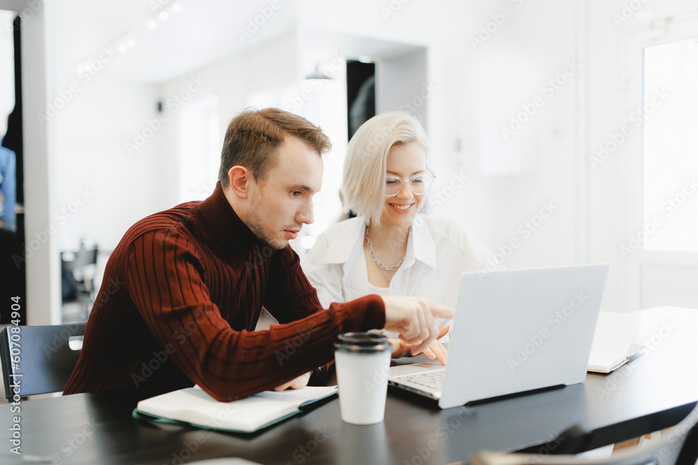 Young creative team working with startup in coworkers, coffee shop. Blonde woman and man work online discussing project together in university using laptop computer Young creative team working with startup in coworkers, coffee shop. Blonde woman and man work online discussing project together in university using laptop computer