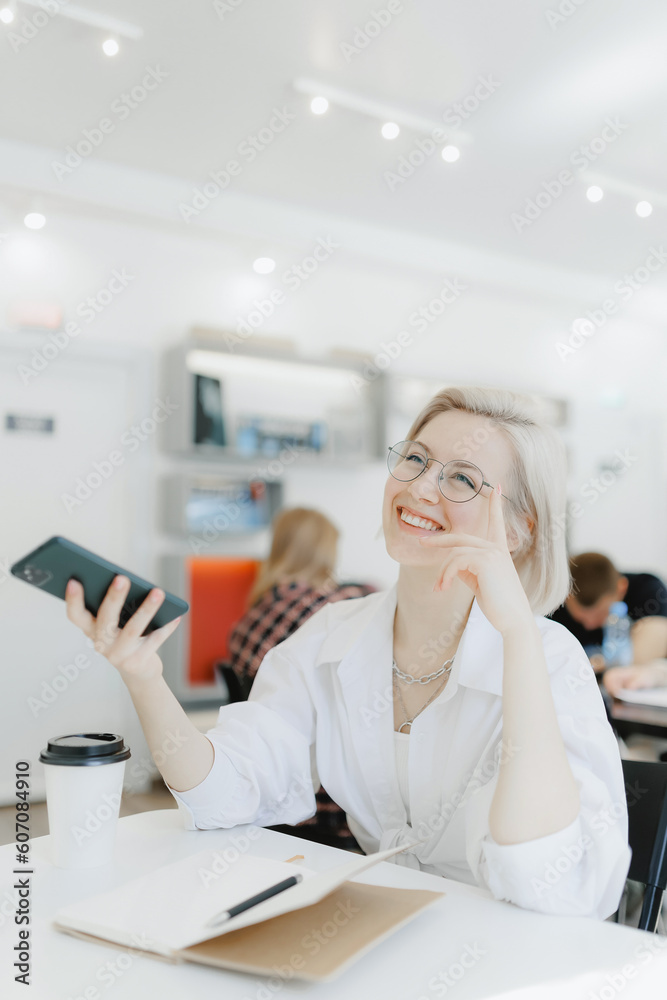 Young woman IT working with phone and notepad in cafe with coffee, white light Young woman IT working with phone and notepad in cafe with coffee, white light