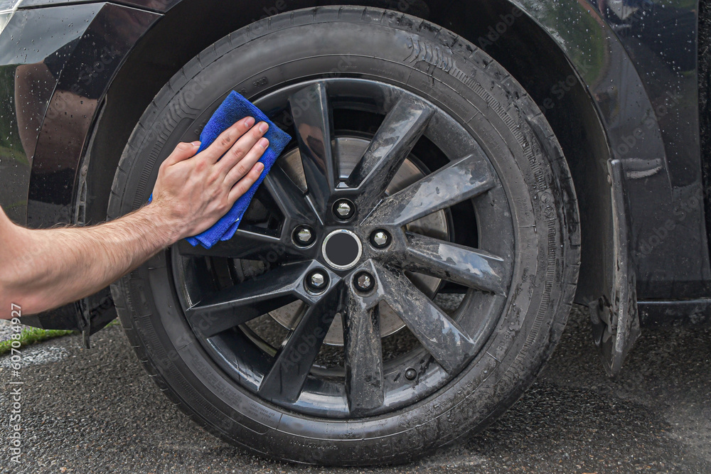 Car wash on the street. Male hand washes a car wheel, close-up