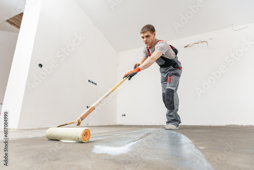 Worker use primer on concrete floor before laying tiles, strengthening surface. Floor priming process