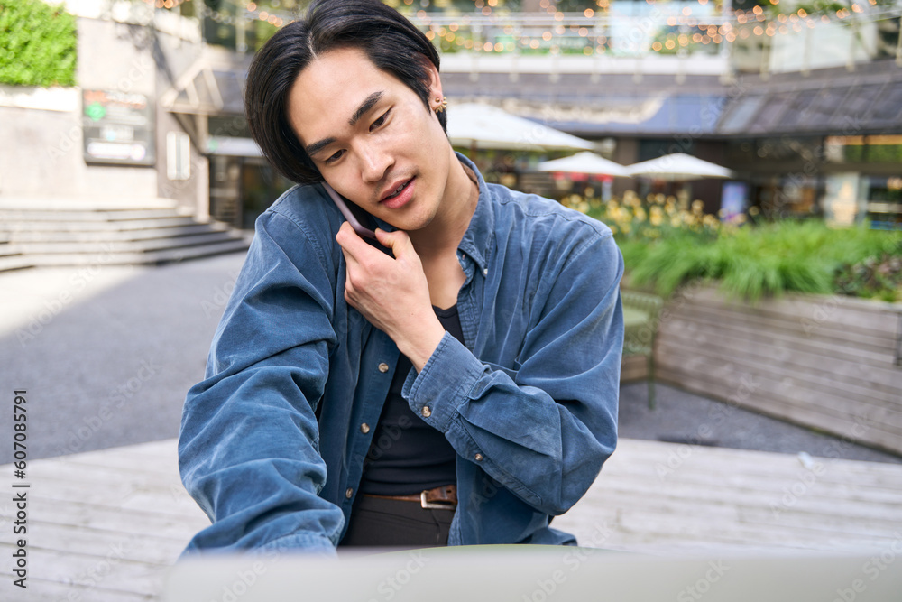 Confident Japanese student using laptop computer, having mobile phone call Confident Japanese student using laptop computer, having mobile phone call