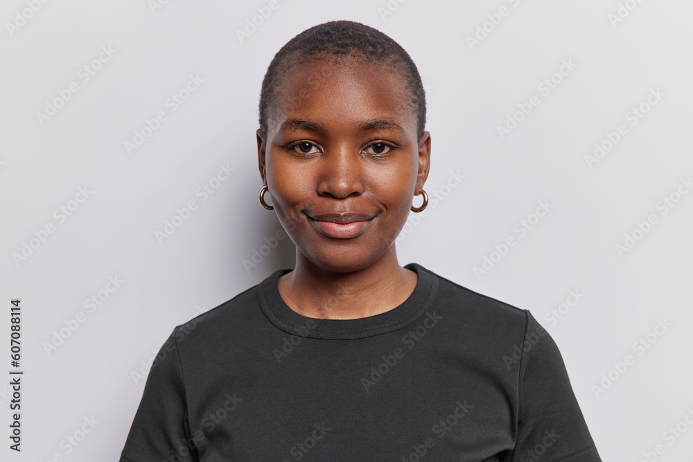 Portrait of pleased dark skinned woman smiles gently looks directly at camera has healthy skin well cared complexion wears casual black t shirt isolated on white background. Human face expressions Portrait of pleased dark skinned woman smiles gently looks directly at camera has healthy skin well cared complexion wears casual black t shirt isolated on white background. Human face expressions