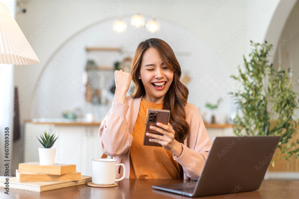 Young smiling asian woman happy relax use laptop conference work,learning education, shopping, study online, webinar, podcast,creative girl holding smartphone positive, success, excited at home