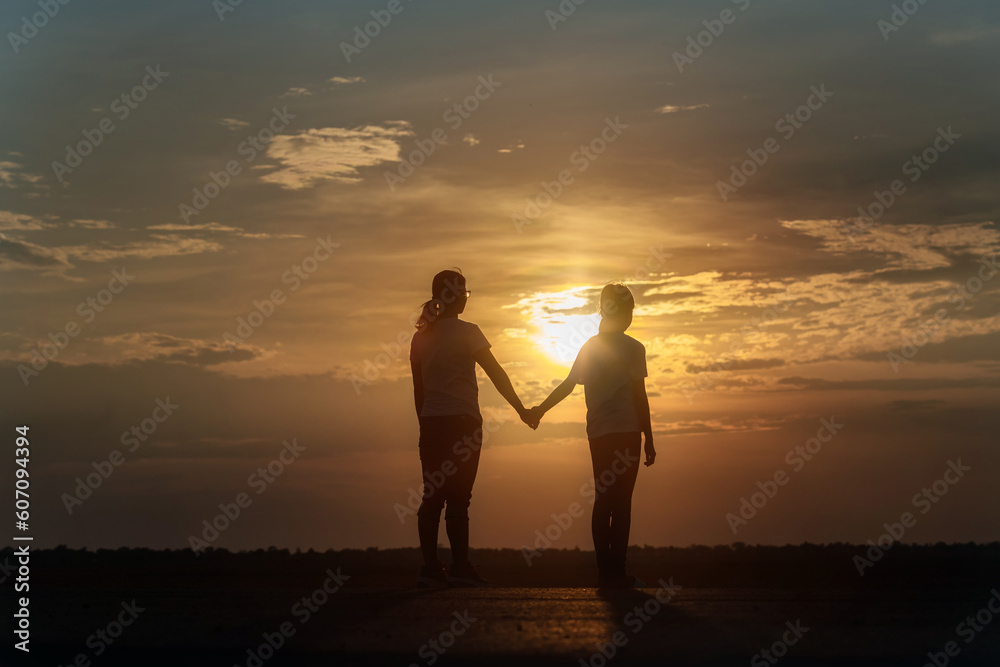 Silhouette of happy family mother and daughter holding hands on sunset background, holiday freedom lifestyle