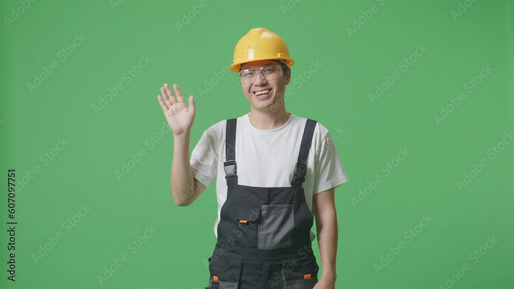 Asian Man Worker Wearing Goggles And Safety Helmet Smiling, Waving Hand, And Saying Bye While Standing In The Green Screen Background Studio
