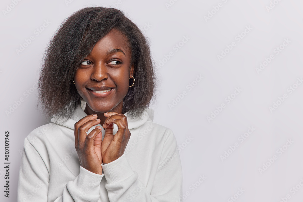 Horizontal shot of dark skinned woman steeples fingers has evil intention to do somethung thinks over scheme looks with cunning expression dressed in casual hoodie isolated over white background - obrazy, fototapety, plakaty 