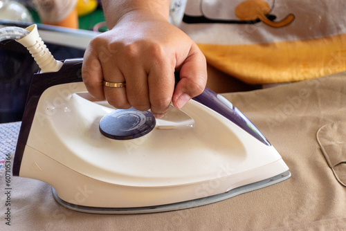 Female hand holding iron to iron clothes on ironing board