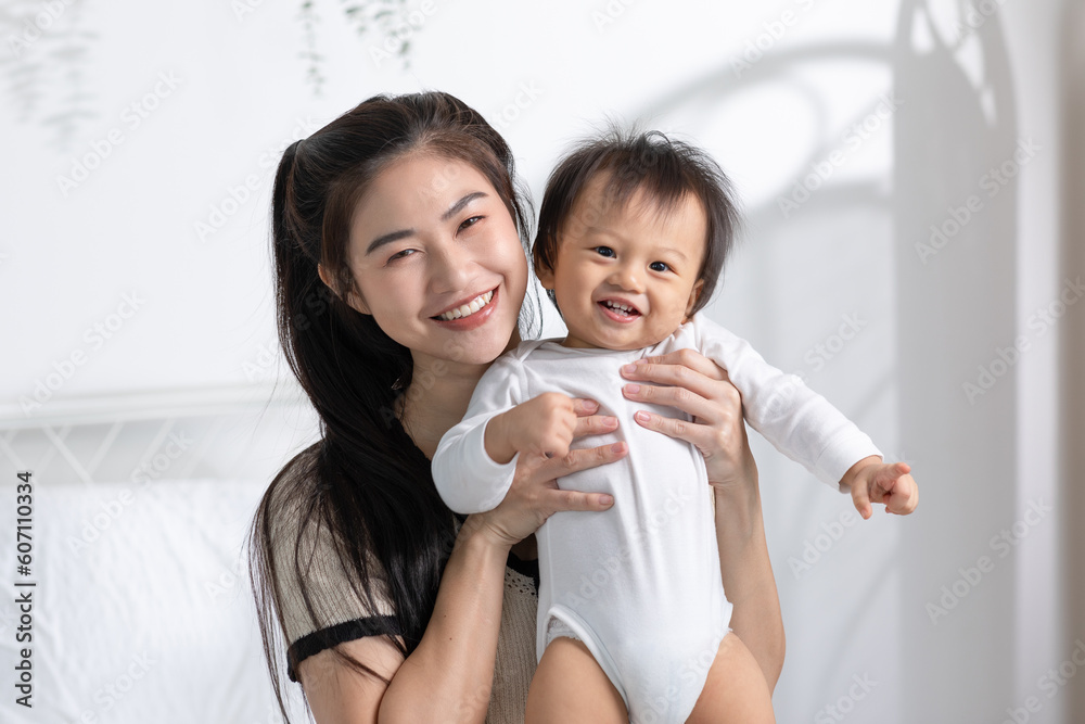 Asian mom holding her baby newborn in hand laughing sweet and lovely. Good moment of Happy mother and infant baby looking together smile with love. Wellness family. Mother and baby newborn Concept Asian mom holding her baby newborn in hand laughing sweet and lovely. Good moment of Happy mother and infant baby looking together smile with love. Wellness family. Mother and baby newborn Concept