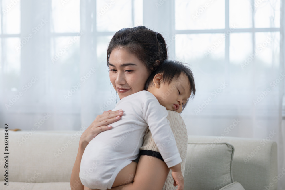 Happy Asian mother holding a cute newborn baby sleep on arm comfort and safety. Happy infant baby sleep with mother standing near windows warm and relax. Good moment. Mom and Baby care Concept Happy Asian mother holding a cute newborn baby sleep on arm comfort and safety. Happy infant baby sleep with mother standing near windows warm and relax. Good moment. Mom and Baby care Concept