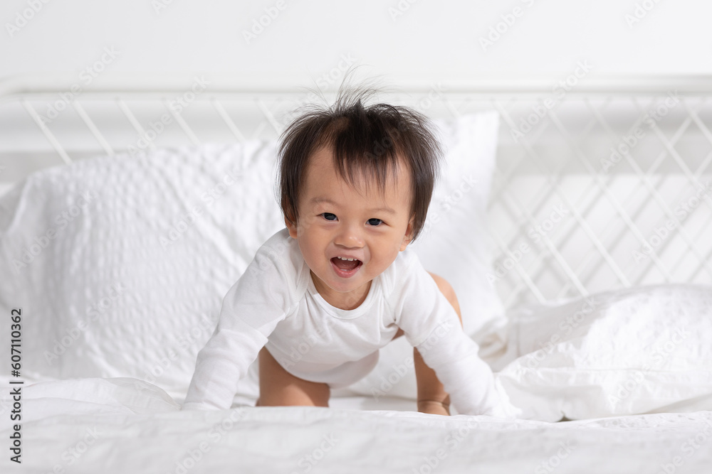Asian baby toddler lying on white bed smile and looking at camera. Happiness little baby playing and practice of tummy time on bed at home. Baby Develop and Growth Concept Asian baby toddler lying on white bed smile and looking at camera. Happiness little baby playing and practice of tummy time on bed at home. Baby Develop and Growth Concept