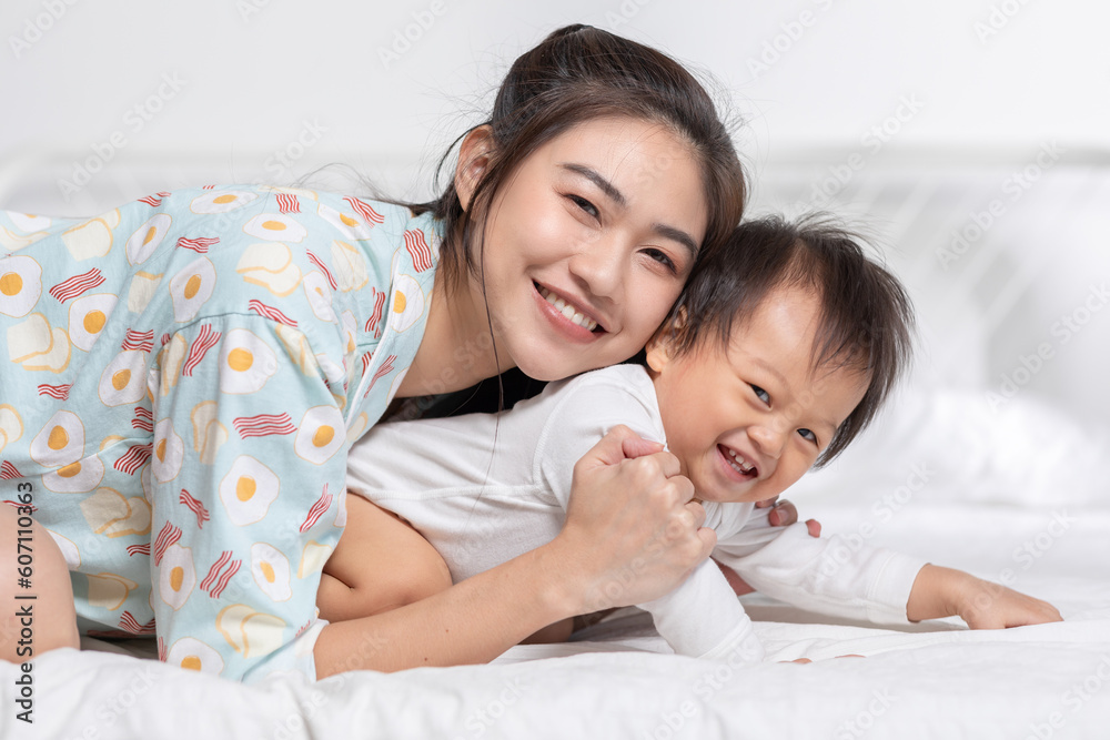 Cute Asian mom hugging her baby boy on bed smile and happiness together. Little baby toddler sit on bed and relax with mother speding time to learning and growth. Good momen of family time. Mother day Cute Asian mom hugging her baby boy on bed smile and happiness together. Little baby toddler sit on bed and relax with mother speding time to learning and growth. Good momen of family time. Mother day