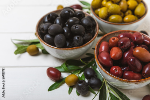 Set of green, red and black olives on a white background. Various types of olives in bowls and olive oil with fresh olive leaves. Delicacy.Mediterranean Kitchen. Copy space.
